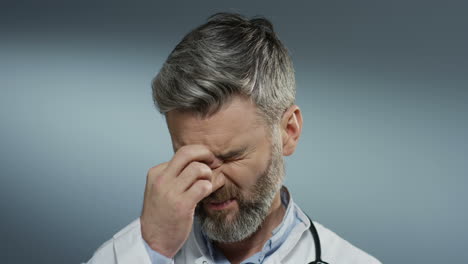 Close-up-of-the-tired-male-doctor-with-gray-hair-putting-stethoscope-on-his-neck-and-taking-off-glasses-after-hard-working-day.